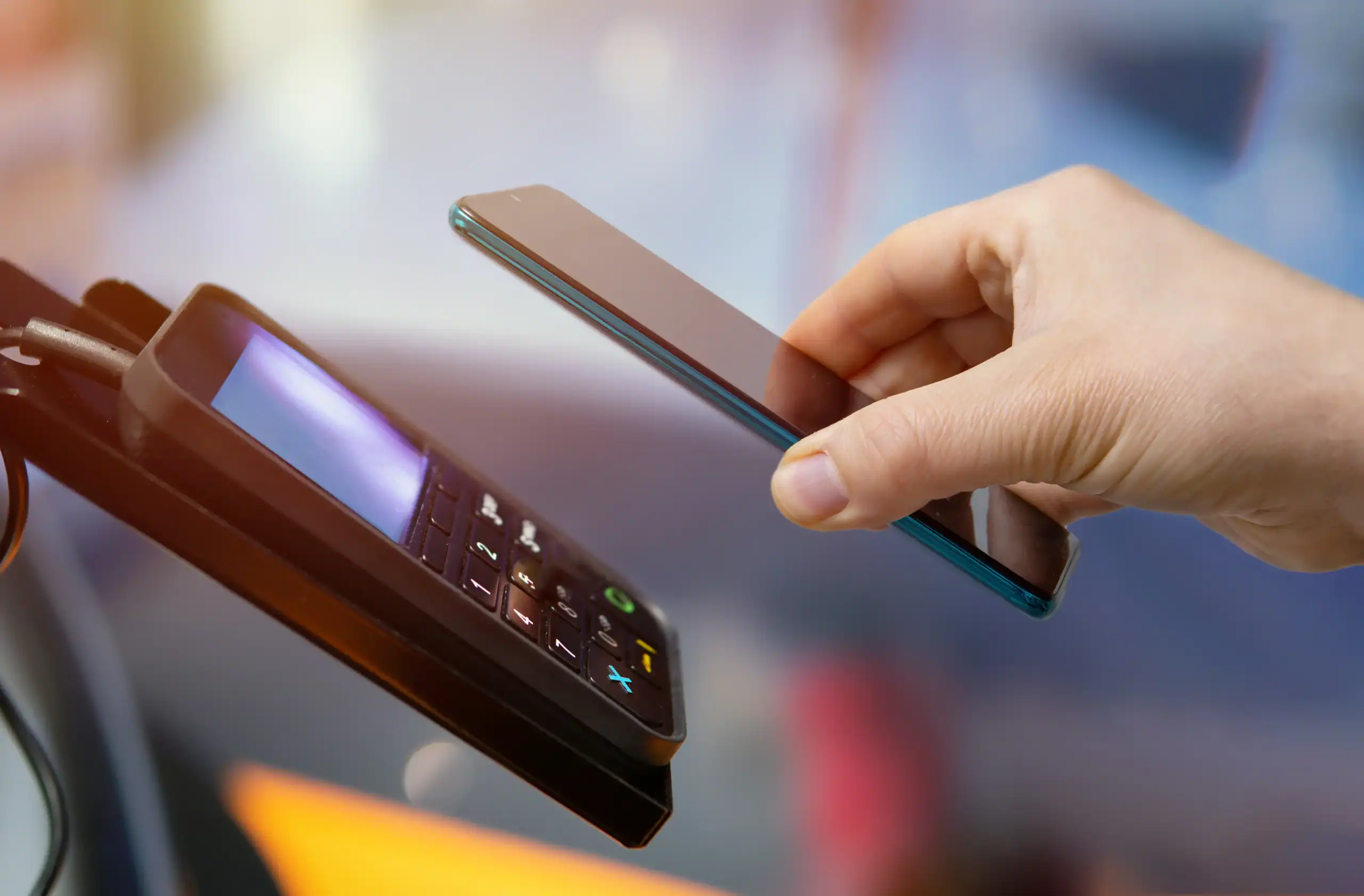 A person using a smartphone to make contactless payment on a card reader.