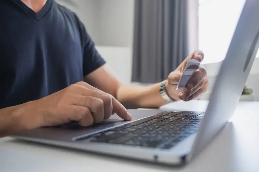 Image of a person using a laptop and credit card for online payments at a desk.